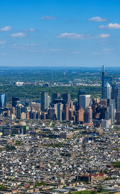 Aerial view of the Philadelphia skyline rising above the dense rowhouse grid seen from Southwest Center City.