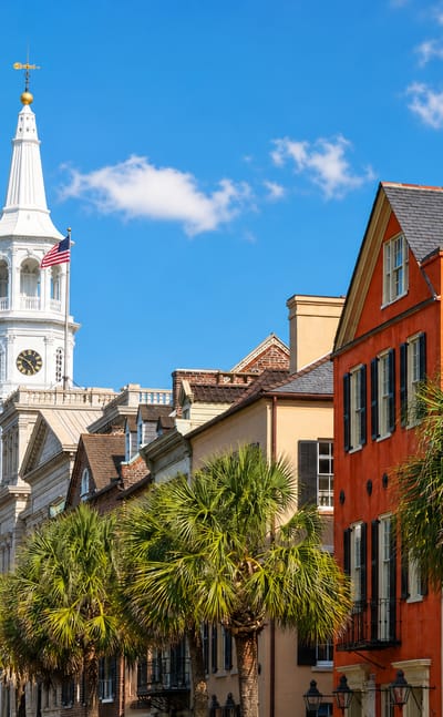 St. Michael's Church steeple rising above colorful historic houses and palmetto palms in Charleston.