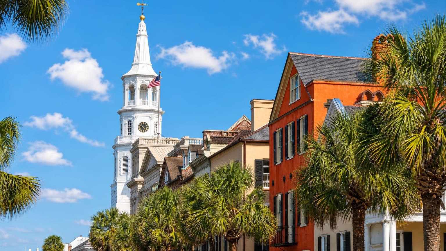 St. Michael's Church steeple rising above colorful historic houses and palmetto palms in Charleston.