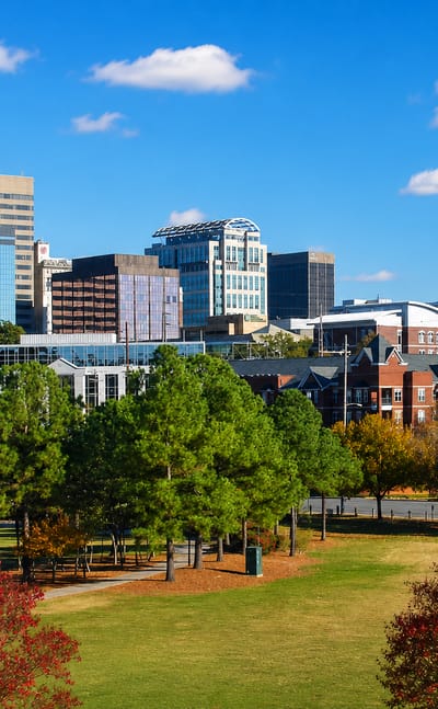 Downtown Columbia, South Carolina skyline rising above Finlay Park's autumn trees under a clear blue sky.