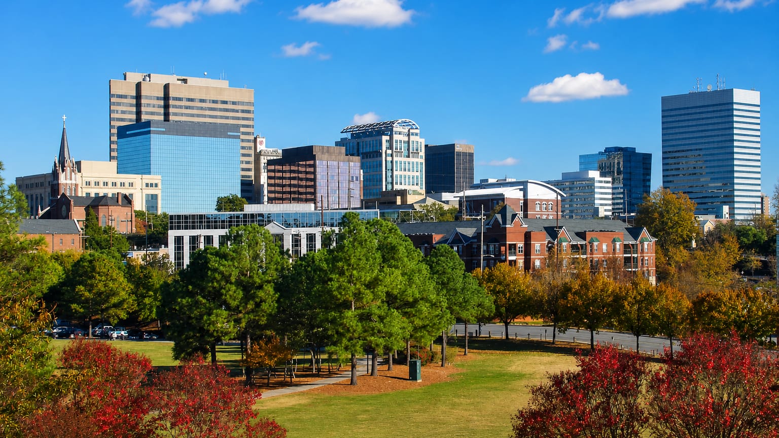 Downtown Columbia, South Carolina skyline rising above Finlay Park's autumn trees under a clear blue sky.