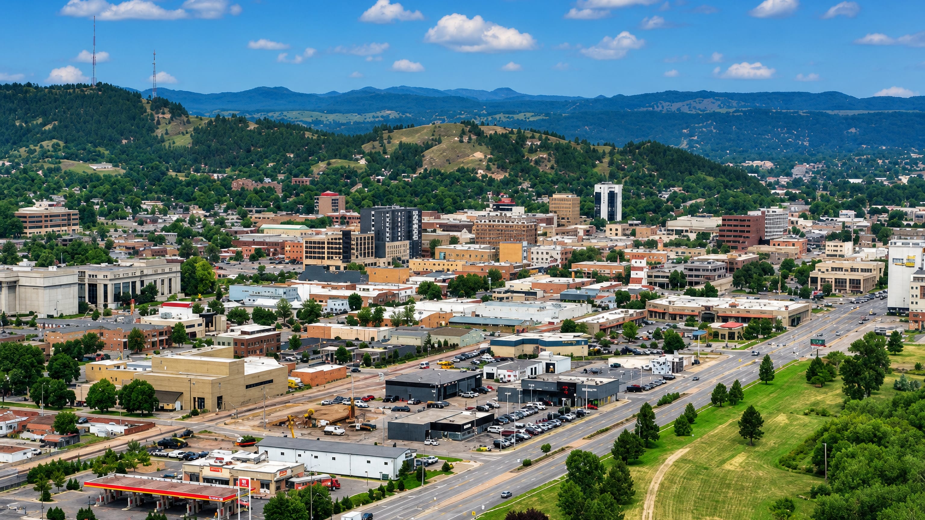 Downtown Rapid City, South Dakota, spread below the pine-covered Black Hills foothills on a clear summer day.