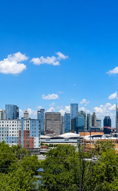 Nashville downtown mid-rise skyline seen above a line of green trees under a blue sky
