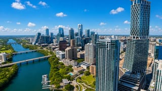 Aerial of downtown Austin skyline along Lady Bird Lake with bridges and glass towers under a clear blue sky.