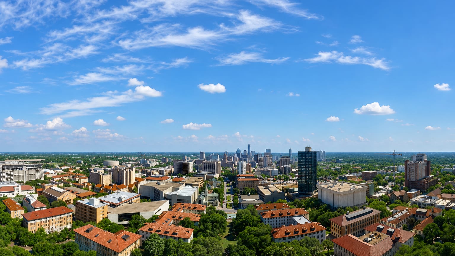 Aerial view of the University of Texas campus with red-tiled roofs and the downtown Austin skyline beyond