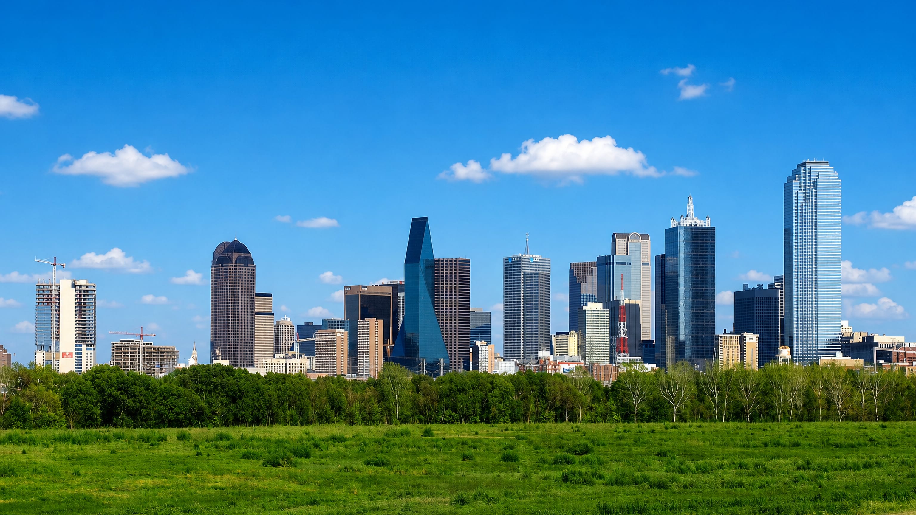 Dallas downtown skyline rising beyond a green field under a bright blue sky