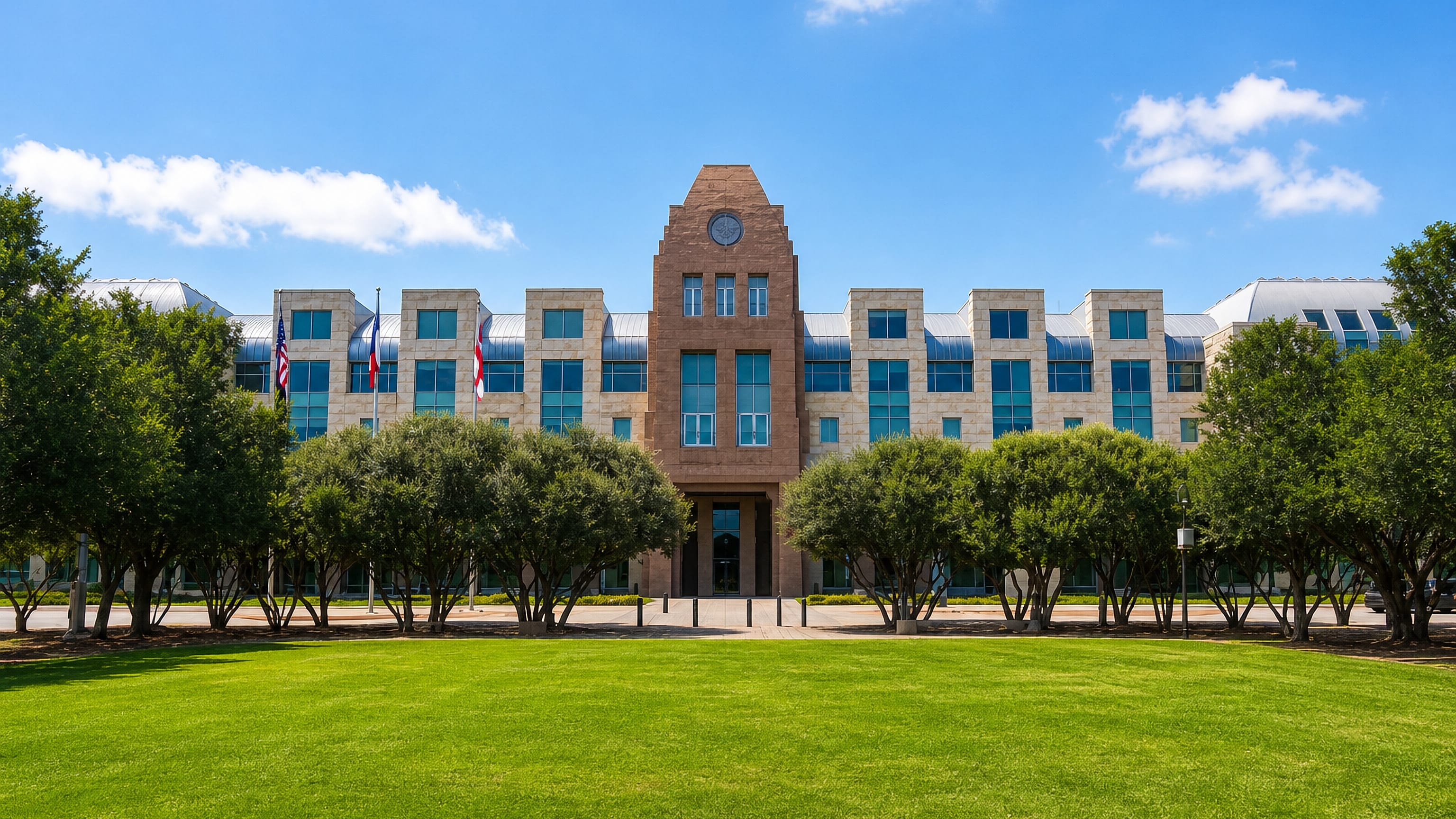 Stone-and-glass municipal building with a clock tower, flagpoles and a wide lawn in Frisco, Texas
