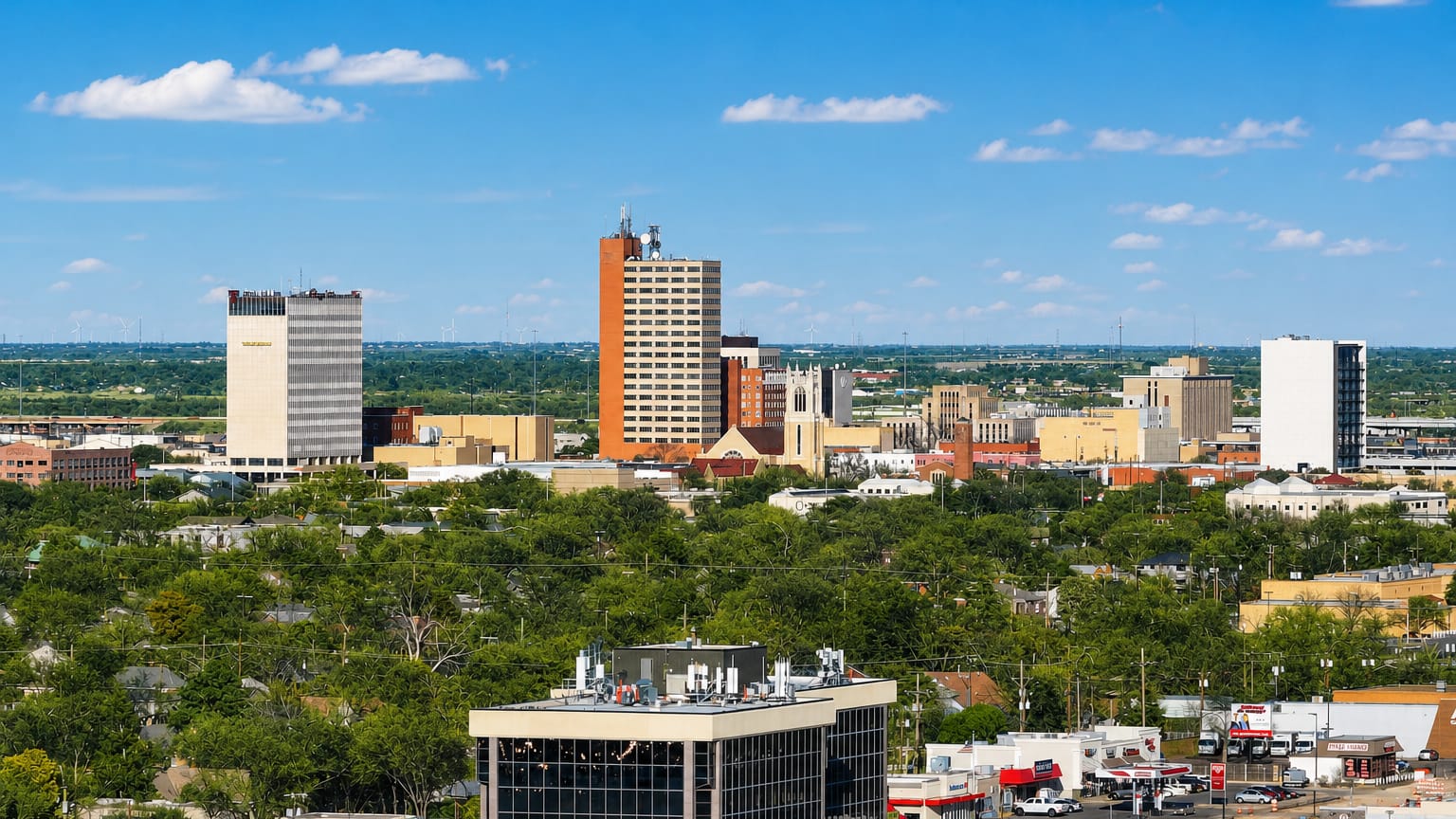 Downtown Lubbock, Texas skyline of low towers rising above green trees and the flat plains under a blue sky.