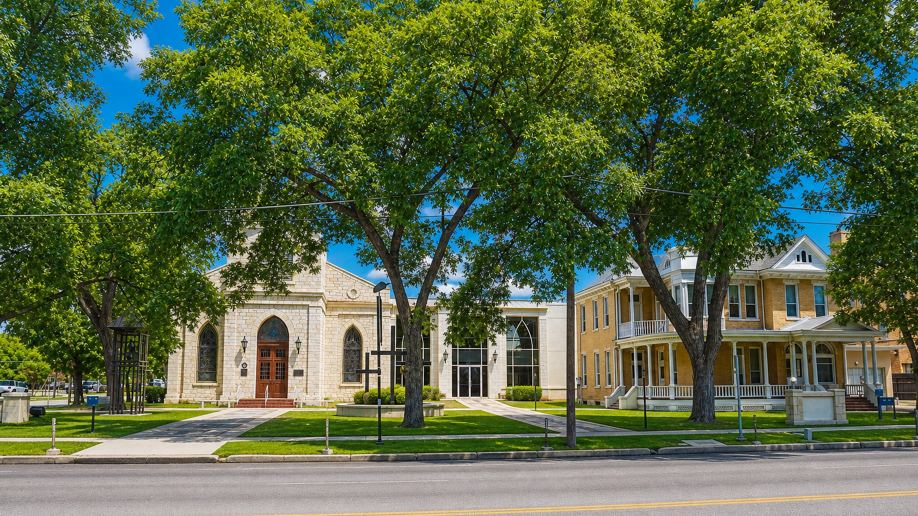 Limestone church and a historic brick house shaded by pecan trees on a street in New Braunfels, Texas