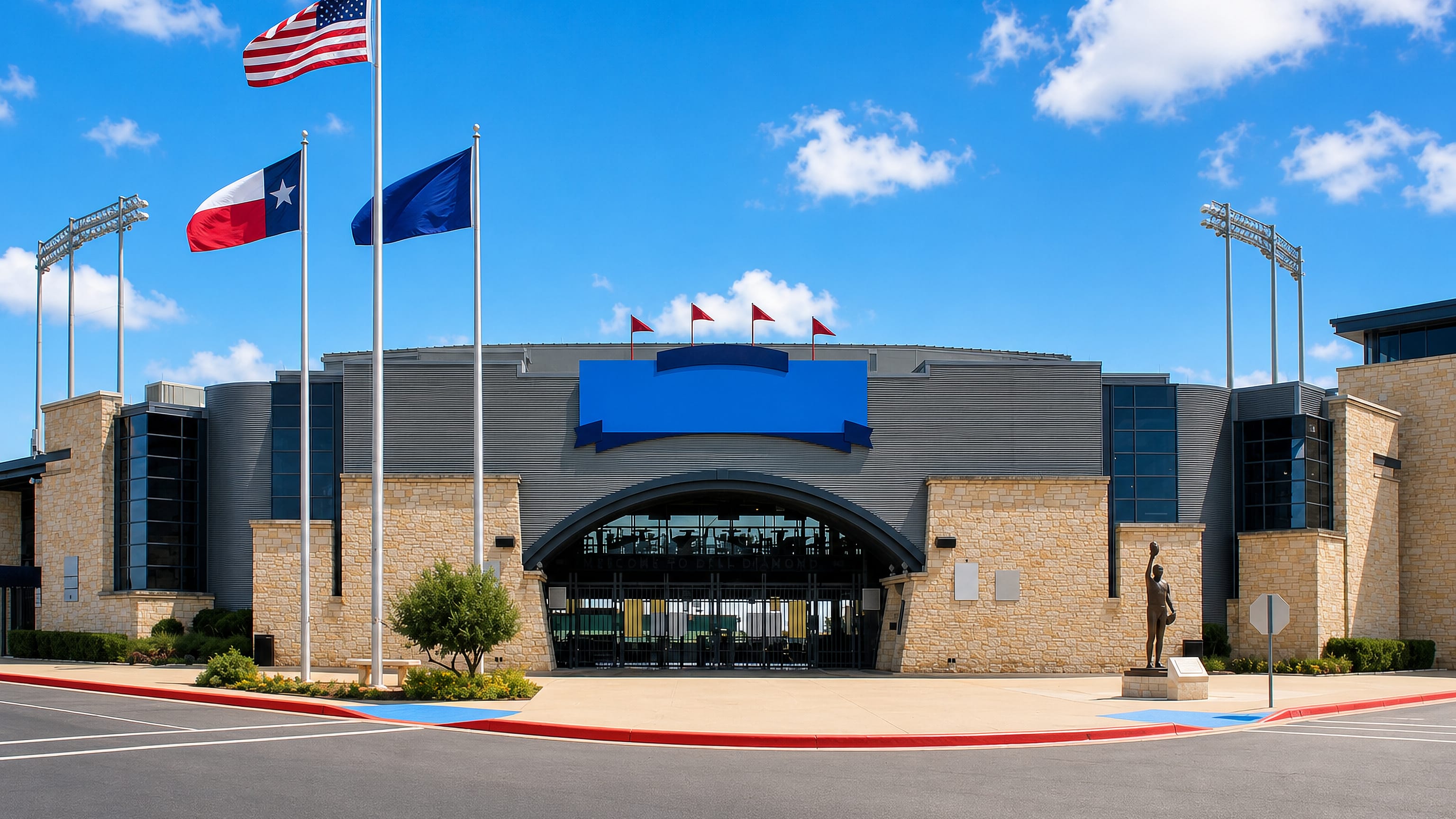 Flag-lined entrance plaza of the ballpark stadium in Round Rock, Texas, under a bright blue sky.
