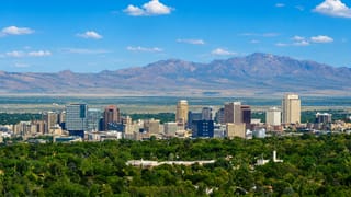 Downtown Salt Lake City skyline backed by the Wasatch Mountains, with green treetops in the foreground.
