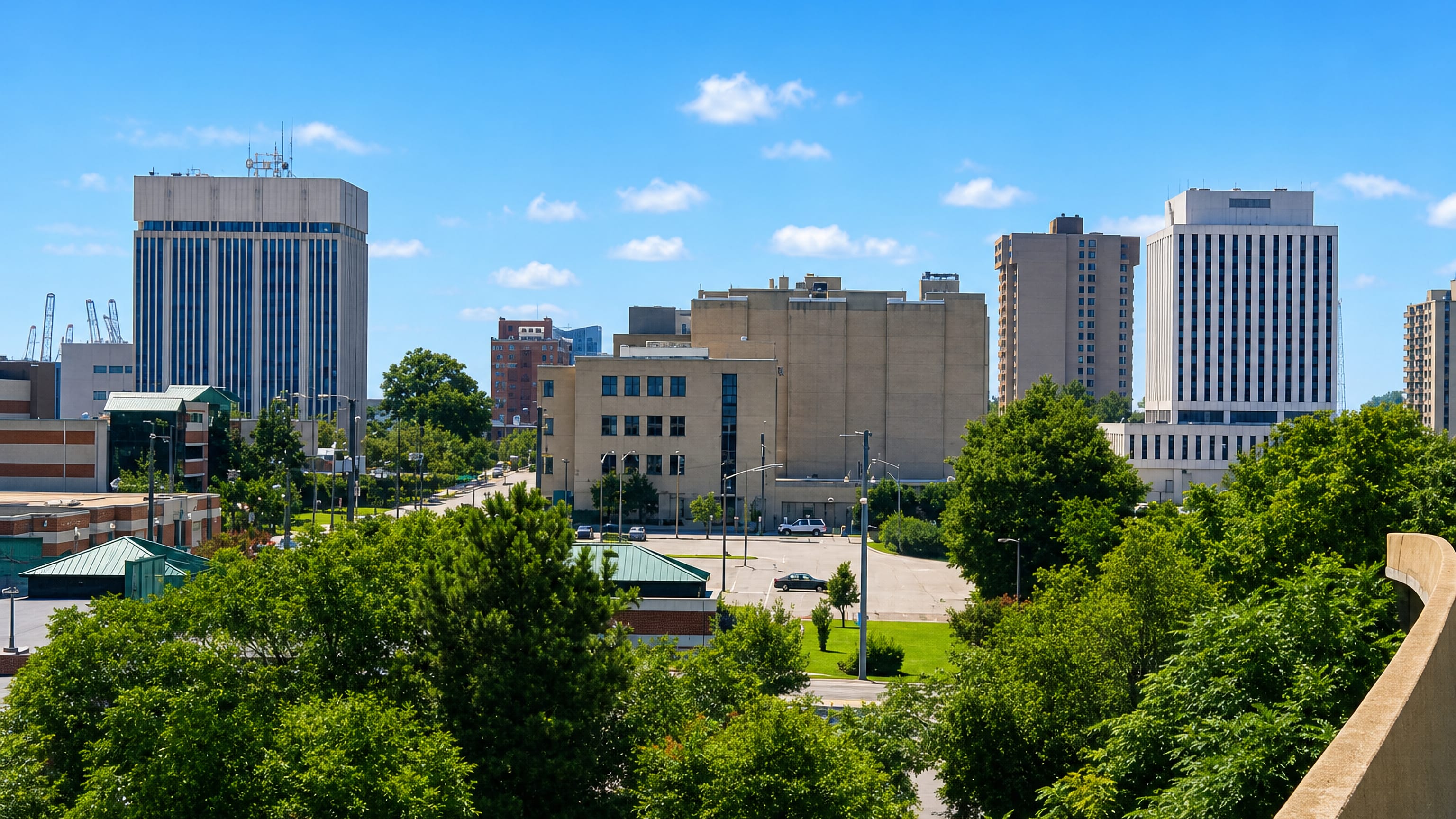 Downtown Newport News, Virginia, mid-rise offices above leafy streets with shipyard gantry cranes on the skyline.