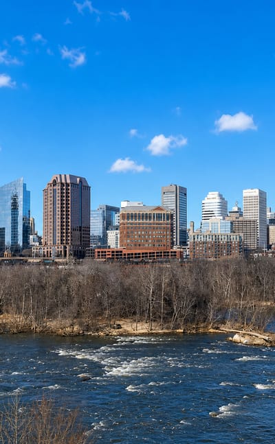 Richmond's downtown skyline rising above the James River rapids and a railroad bridge in Virginia.