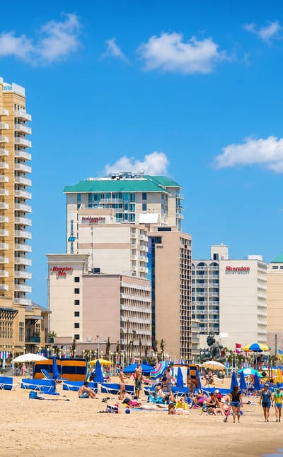 Virginia Beach, Virginia, oceanfront with beachgoers, umbrellas and a row of hotels lining the sandy shore.