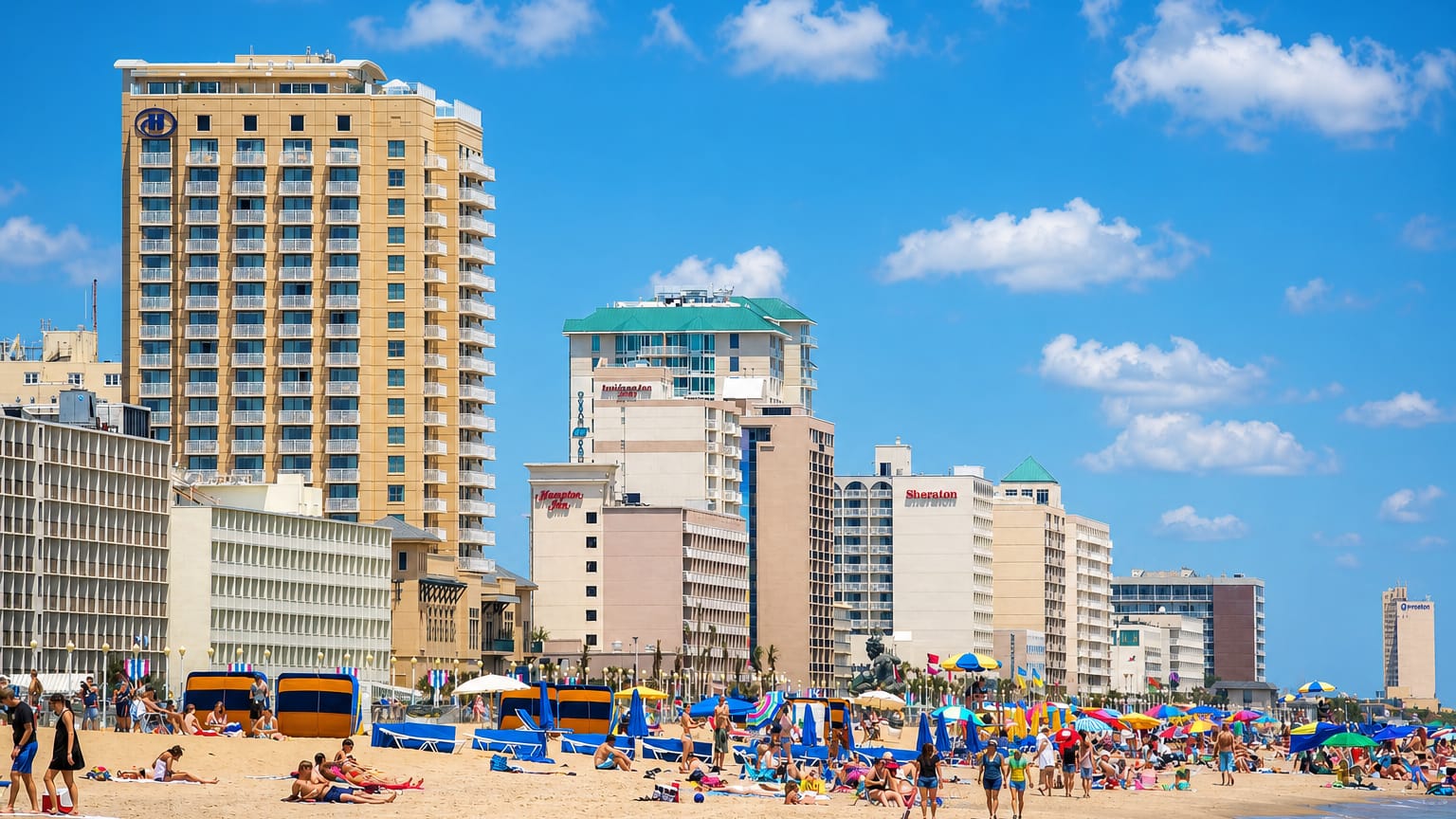 Virginia Beach, Virginia, oceanfront with beachgoers, umbrellas and a row of hotels lining the sandy shore.