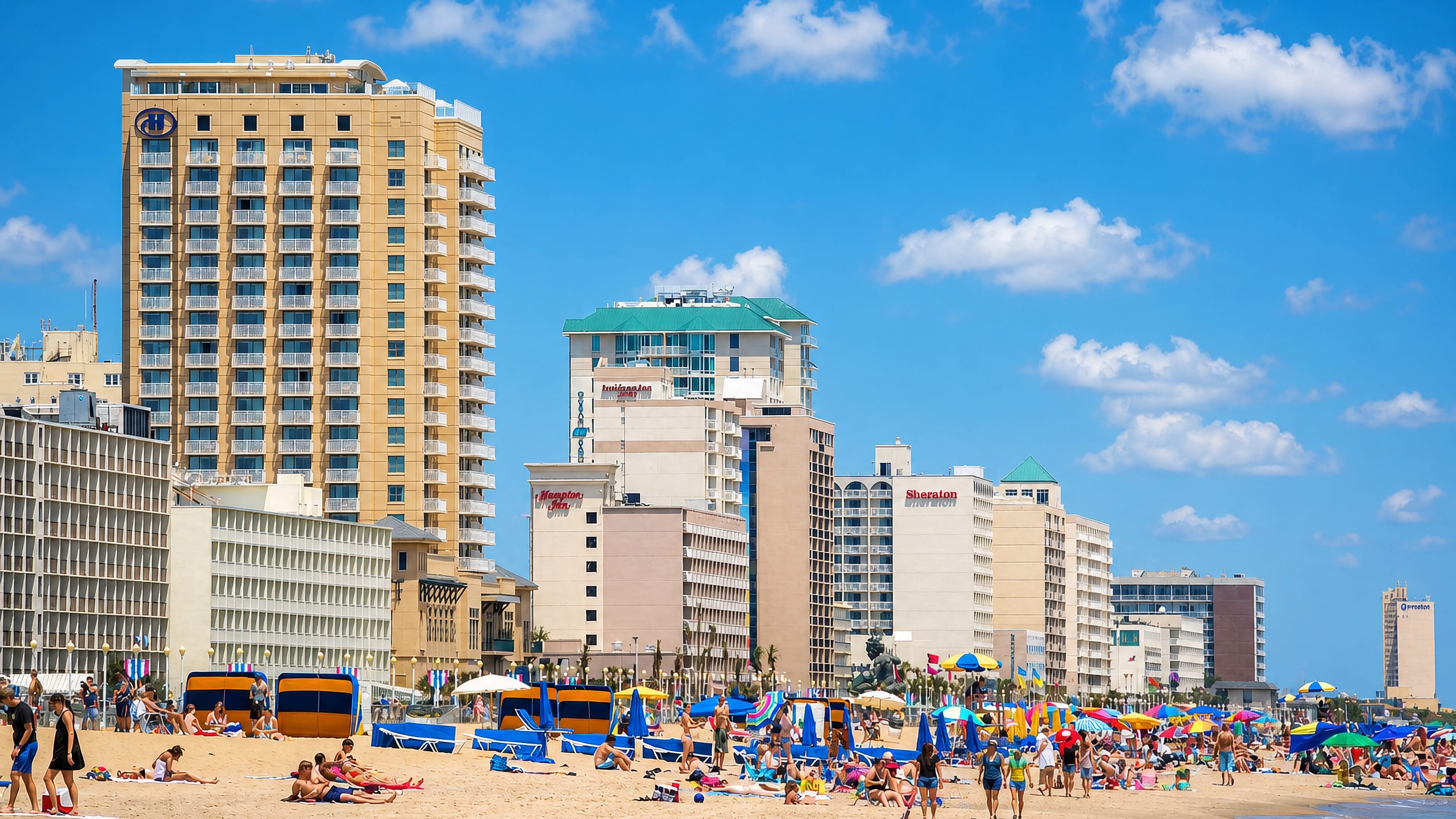 Virginia Beach, Virginia, oceanfront with beachgoers, umbrellas and a row of hotels lining the sandy shore.