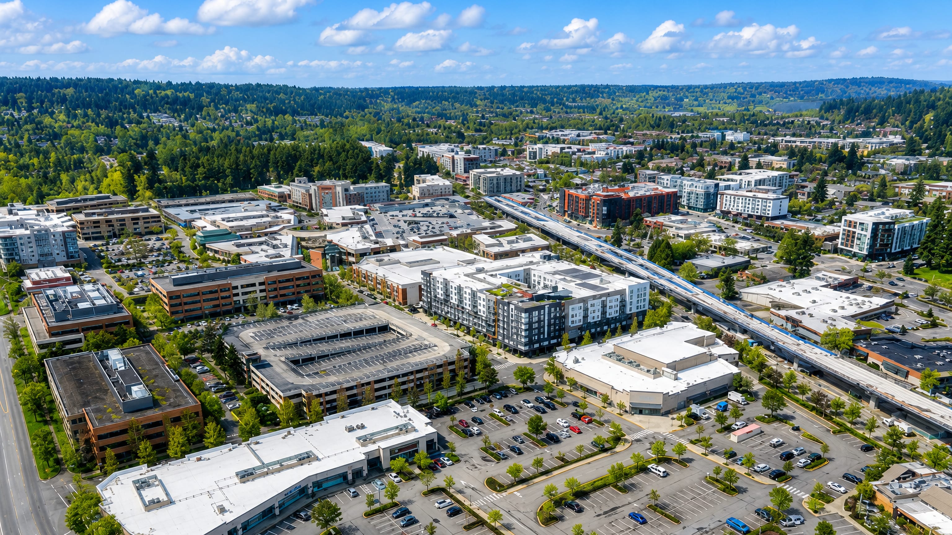 Aerial view of downtown Redmond, Washington, with an elevated light-rail line, low-rise blocks and evergreen forest.