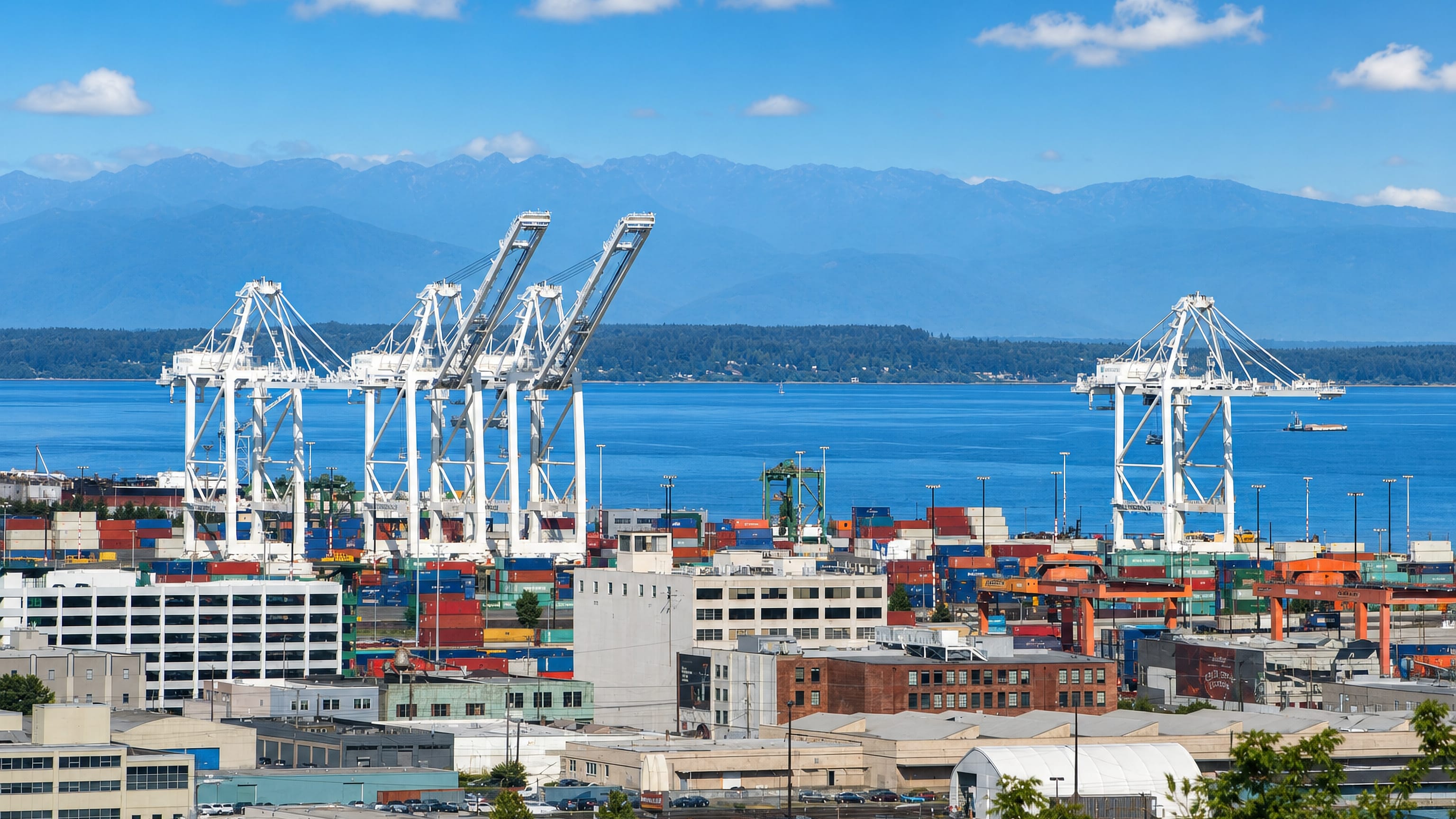 Container cranes and stacked freight in Seattle's SoDo district, with Puget Sound and the Olympic Mountains beyond.