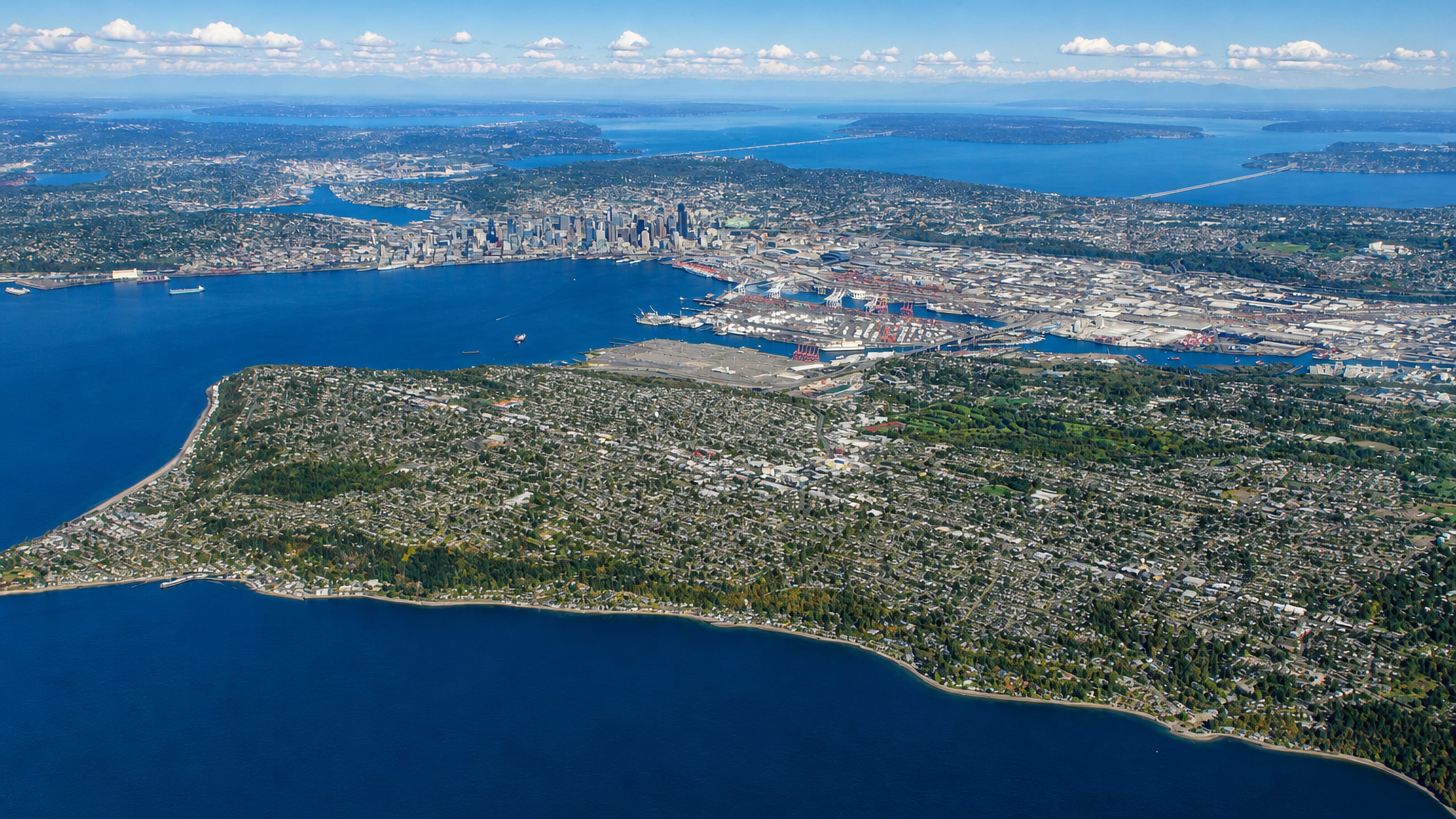 Aerial view over the West Seattle peninsula with its Alki shoreline, Puget Sound and the downtown Seattle skyline beyond.