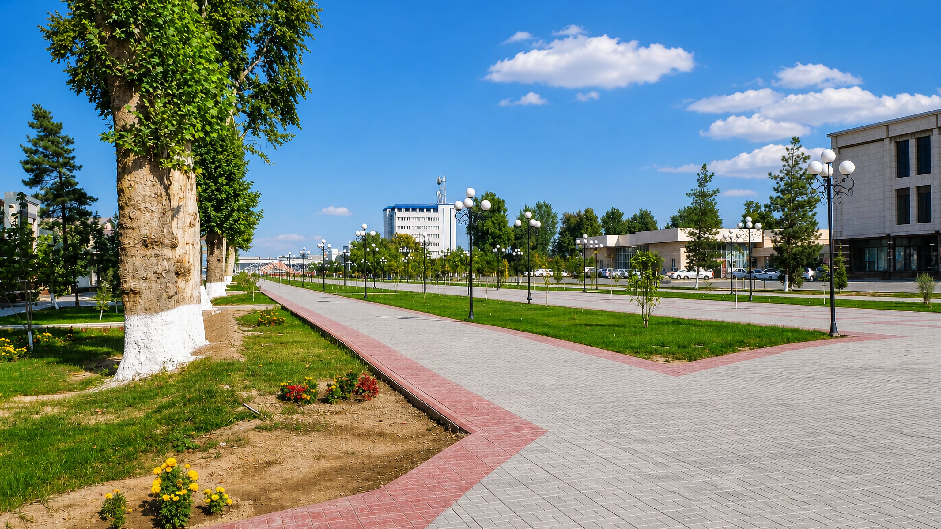 A tree-lined pedestrian boulevard and paved plaza in central Fergana, Uzbekistan, under a bright summer sky.