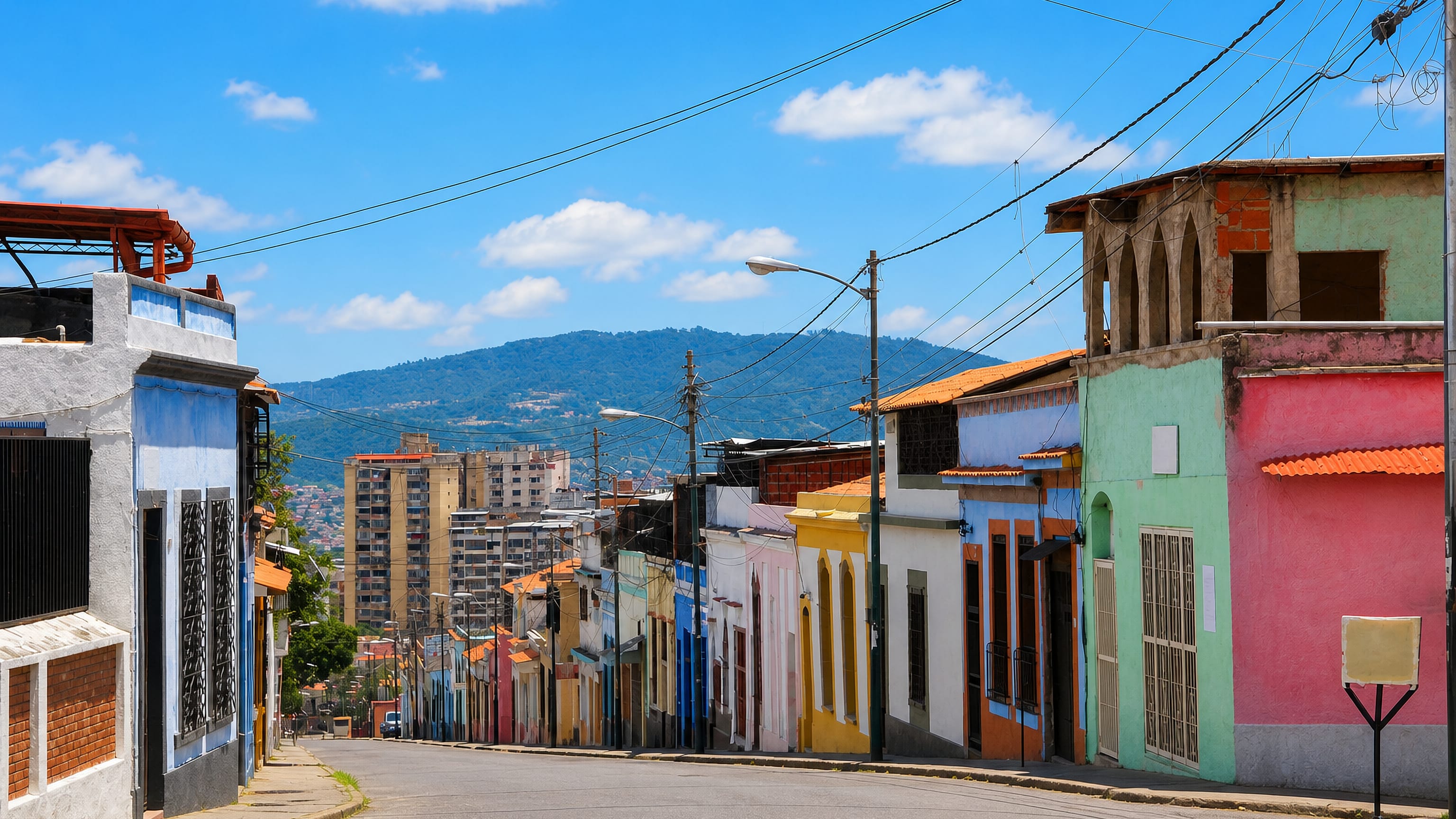 Colourful low-rise houses lining a hillside street in La Pastora, Caracas, with mountains beyond.