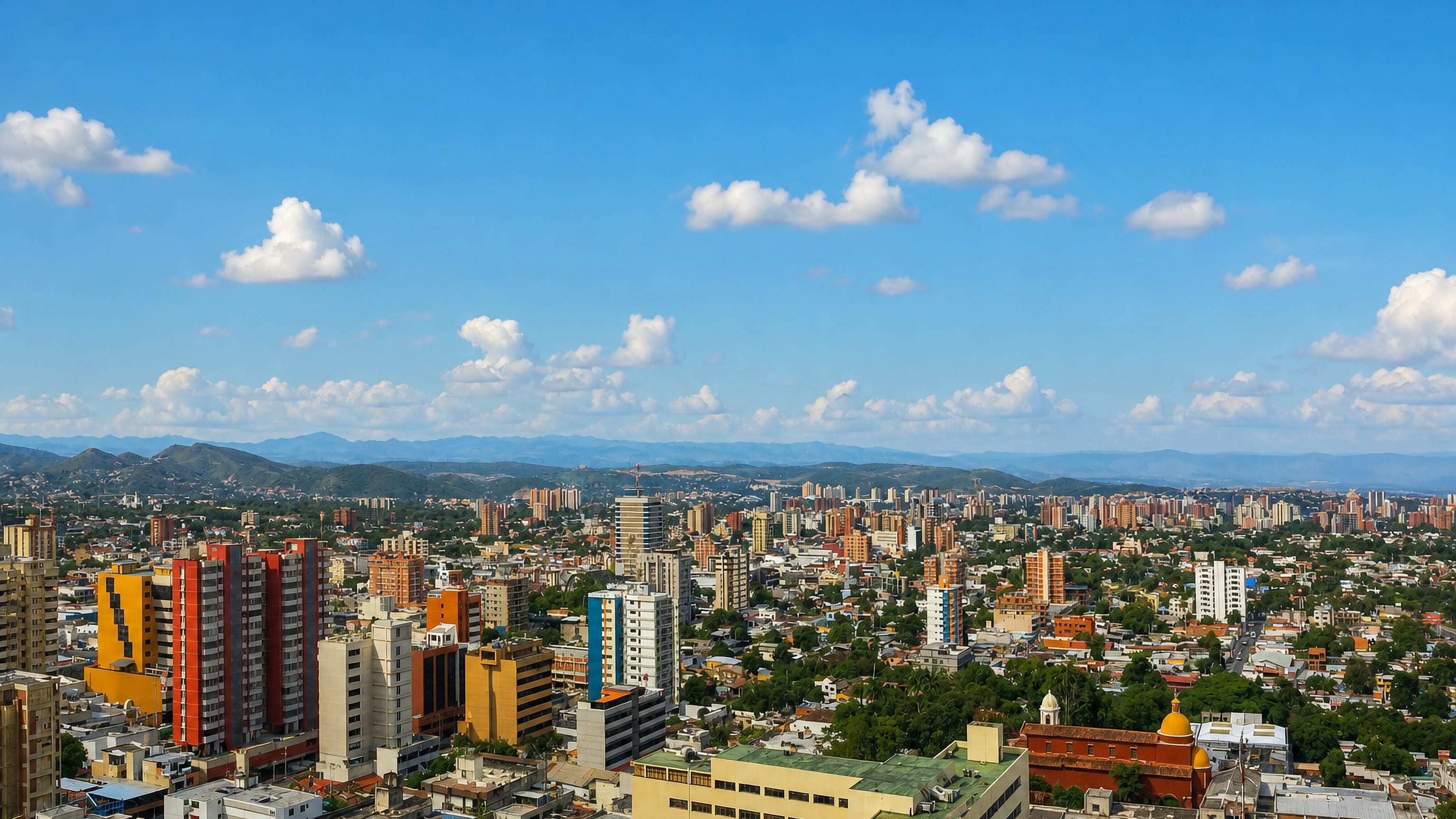 Aerial view of Barquisimeto's colourful mid-rise blocks and red rooftops spreading toward distant hills.