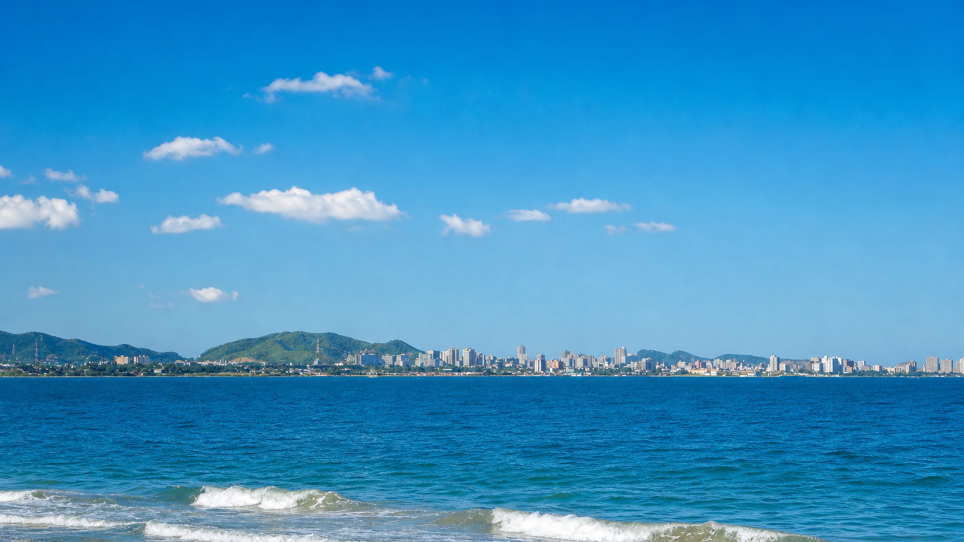 The skyline of Porlamar seen across the blue waters of Margarita Island's bay, with green hills behind.