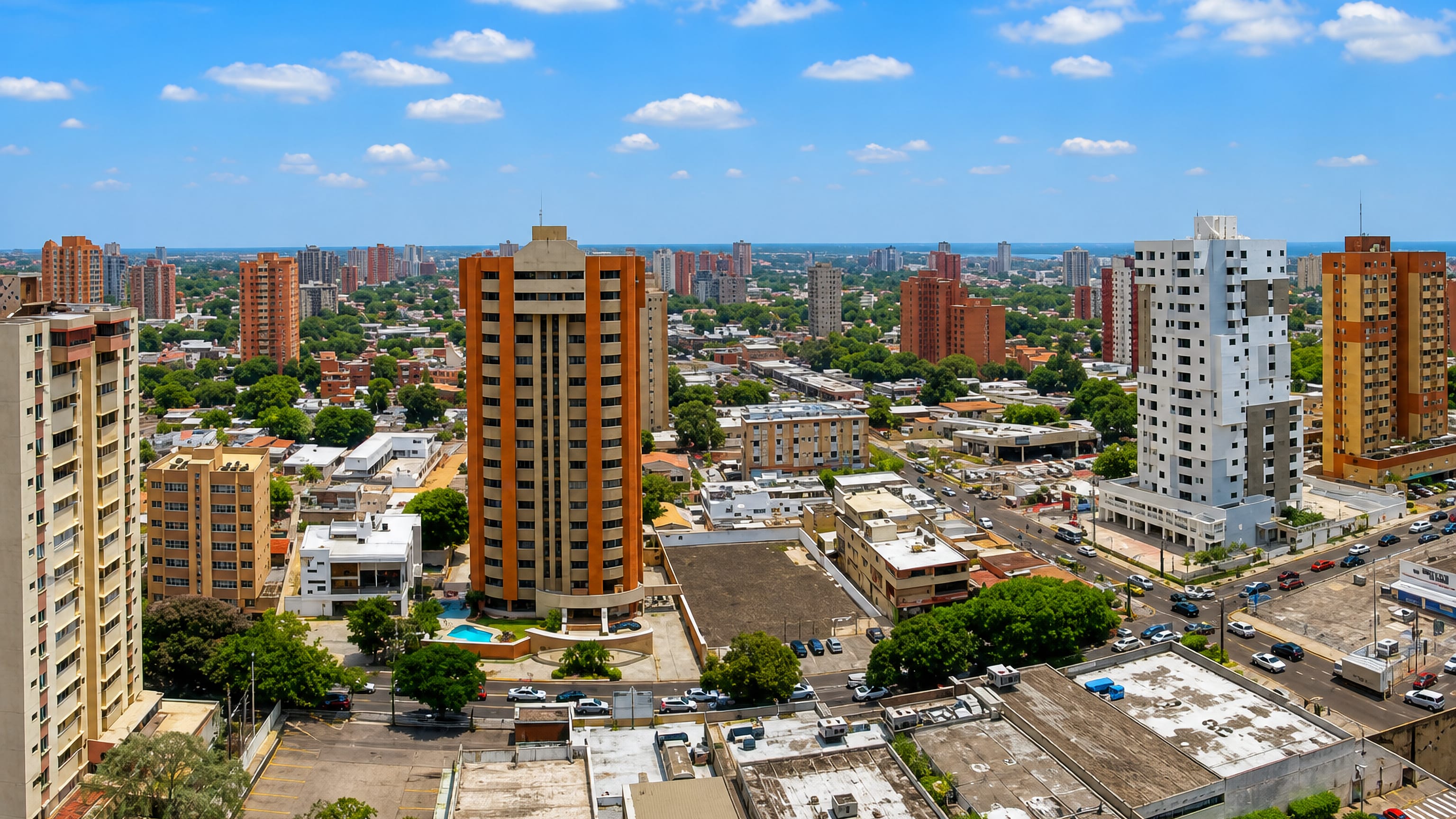 Aerial view over Maracaibo's mid-rise apartment towers and tree-lined avenues, with the lake on the far horizon.