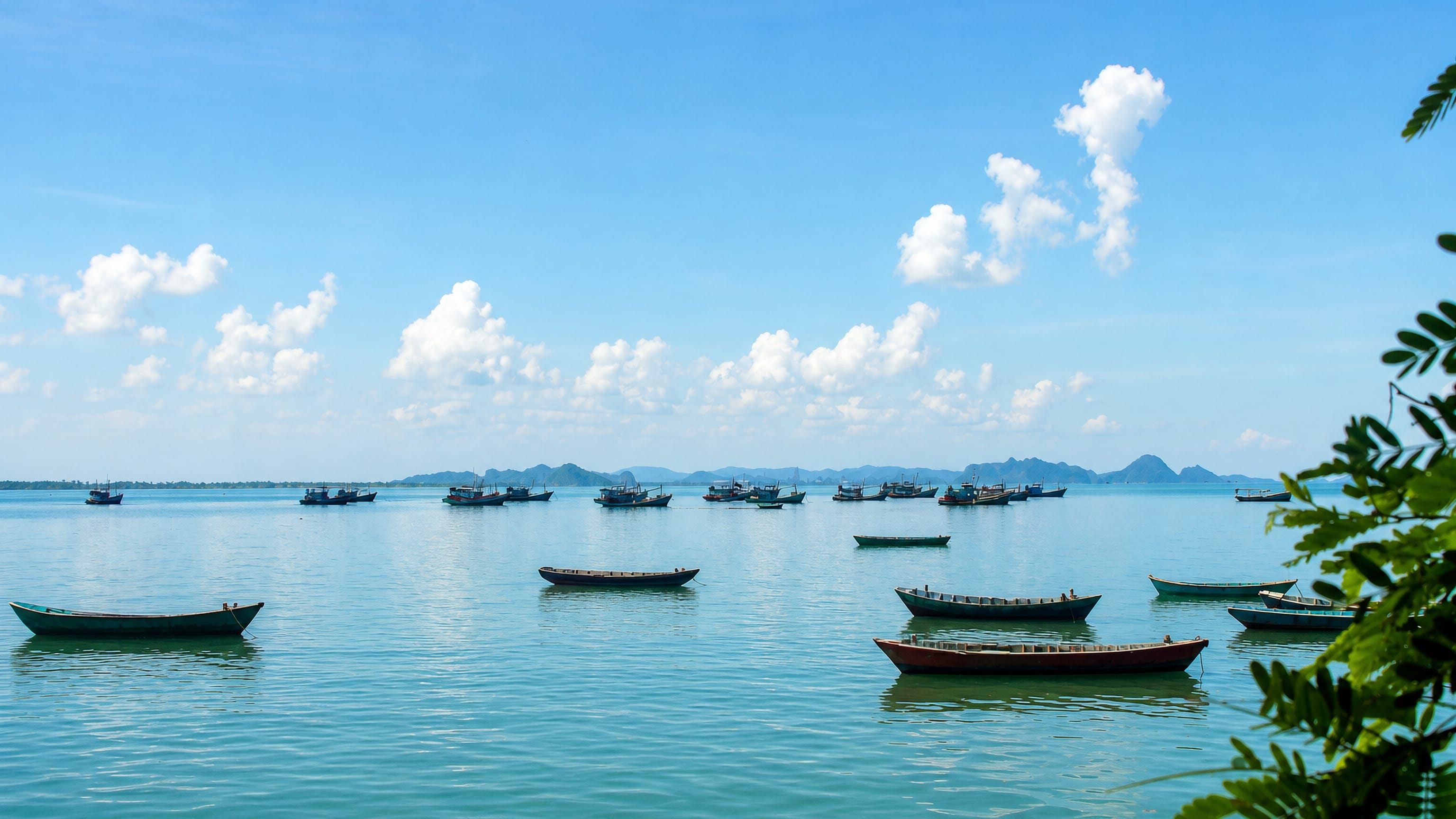 Wooden fishing boats moored on the calm turquoise sea off Ha Tien, Vietnam, with karst islets beyond