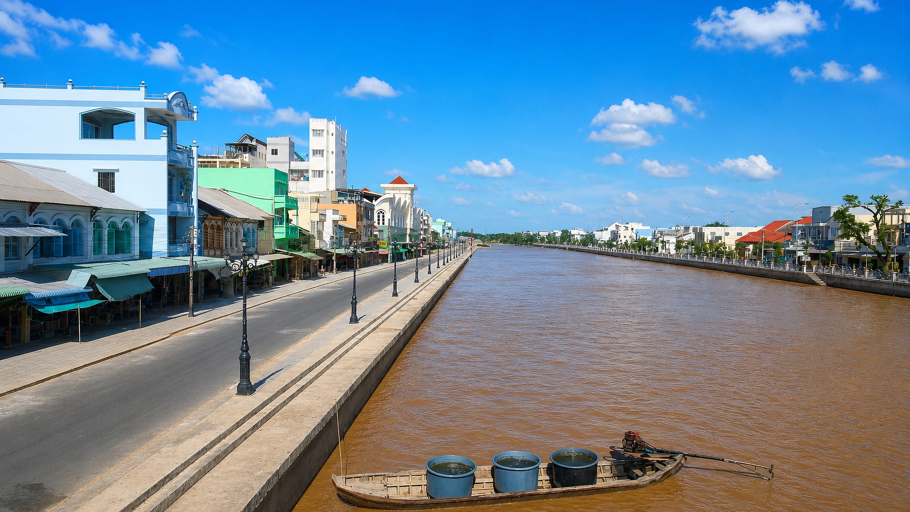 Bạc Liêu's riverside street of shophouses along a canal embankment with a laden sampan below