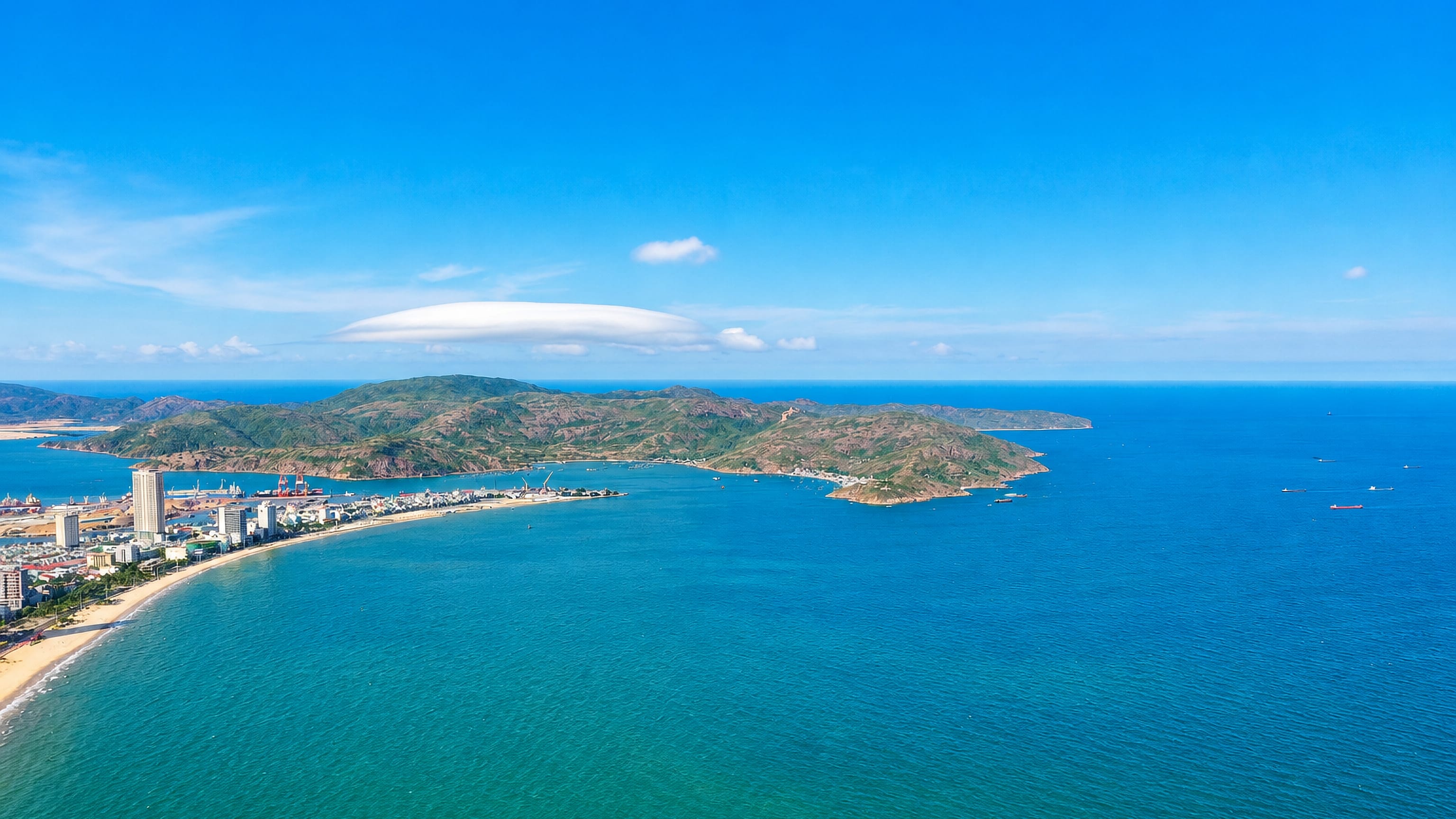 Aerial view of Qui Nhon, Vietnam: a crescent beach and high-rises curving toward a green headland and blue sea