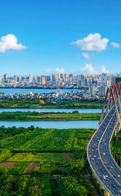 Hanoi skyline beyond the Red River floodplain, with a cable-stayed bridge and the Keangnam Landmark 72 tower on the horizon