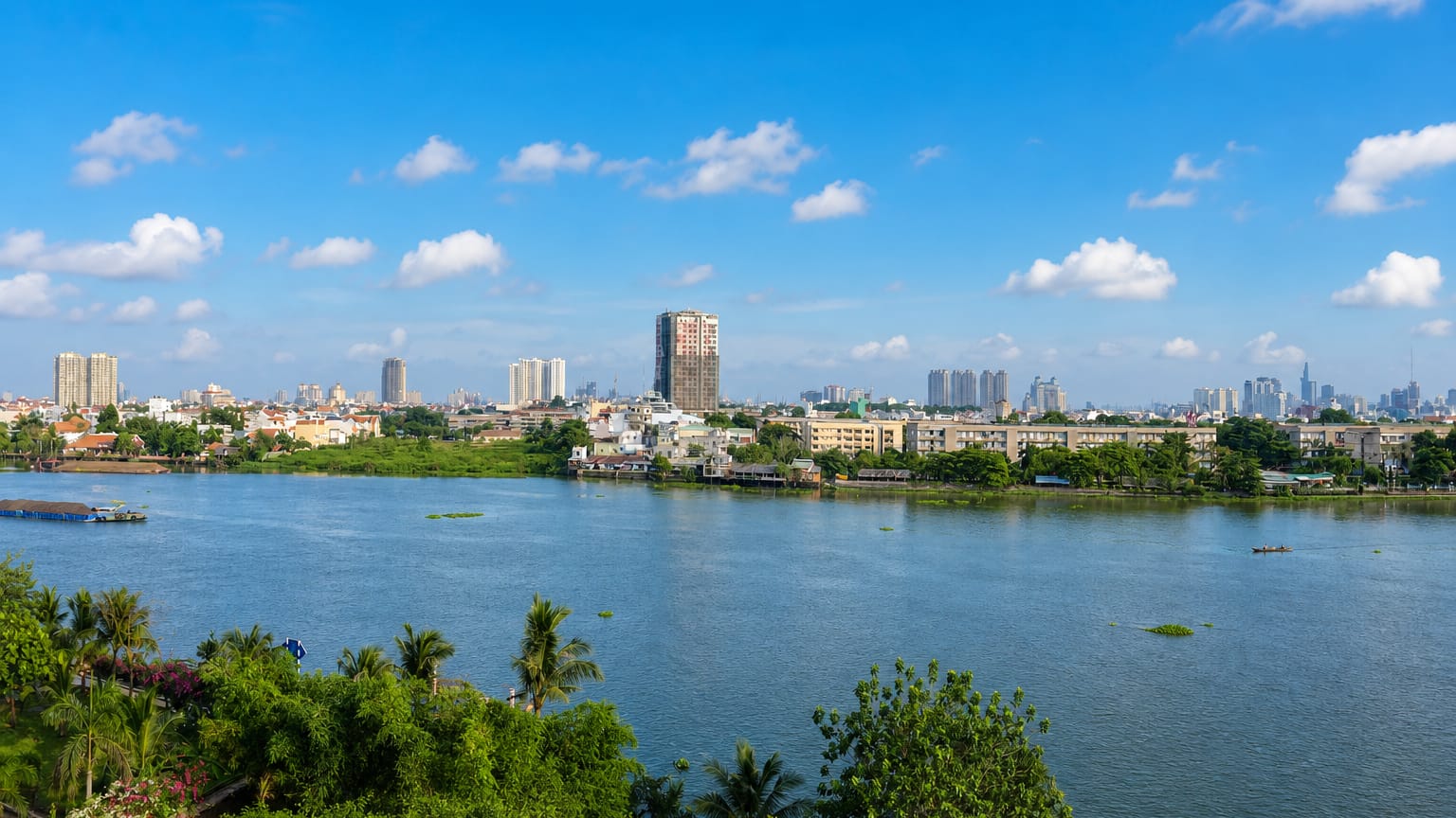 Saigon River waterfront in Binh Thanh, Ho Chi Minh City, with high-rise towers rising behind riverside greenery.