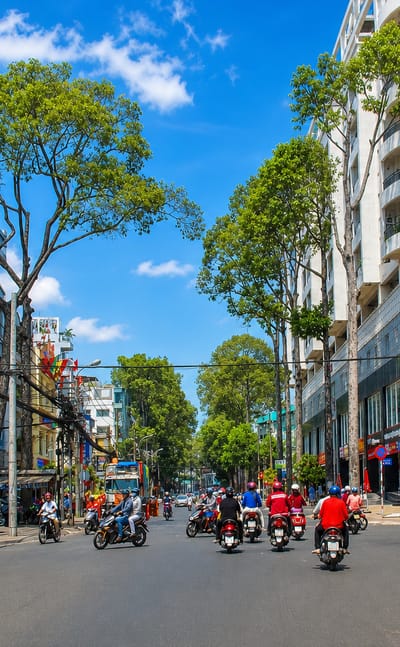 Motorbike-filled street with shophouses and a curved modern building in Ho Chi Minh City's Cholon district