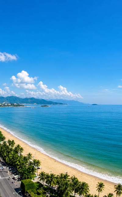Palm-lined Tran Phu beachfront curving along Nha Trang bay past hotels toward distant mountains.