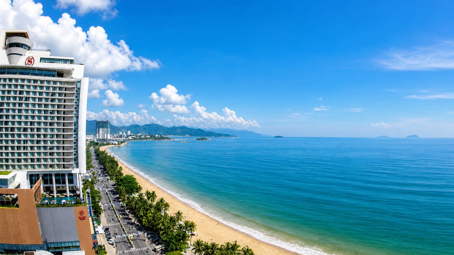 Palm-lined Tran Phu beachfront curving along Nha Trang bay past hotels toward distant mountains.