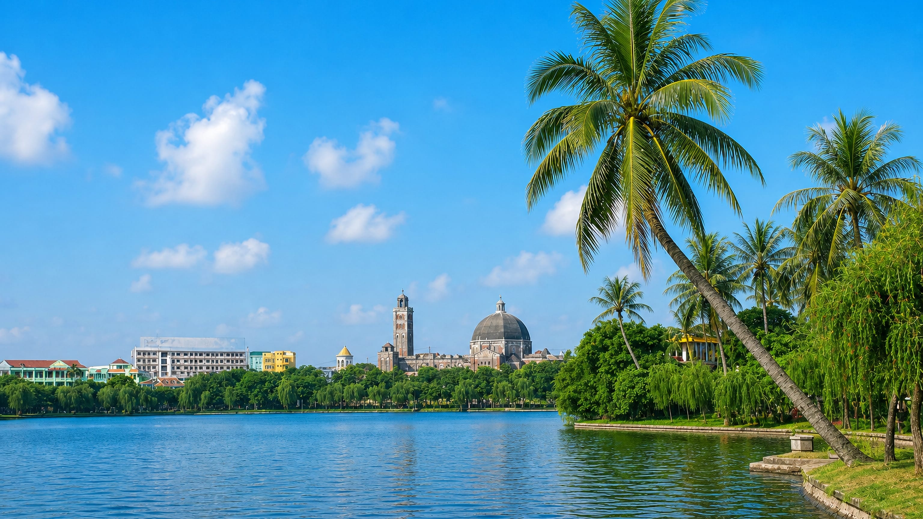 Lakeside view in Nam Dinh, Vietnam, palms and willows framing a domed church and bell tower across the water.