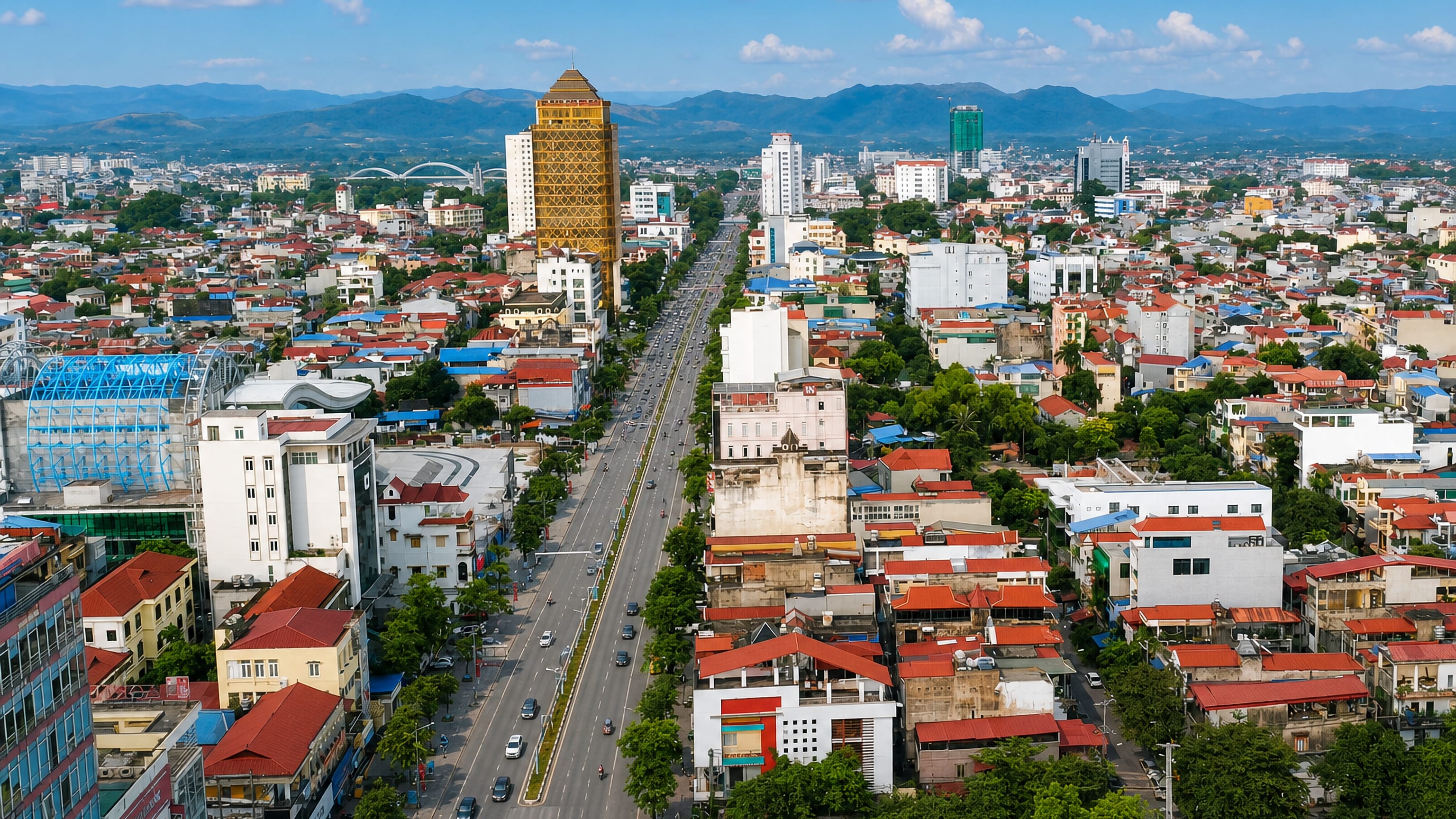 Aerial view of Thái Nguyên, Vietnam, a wide boulevard and golden tower framed by distant mountains.
