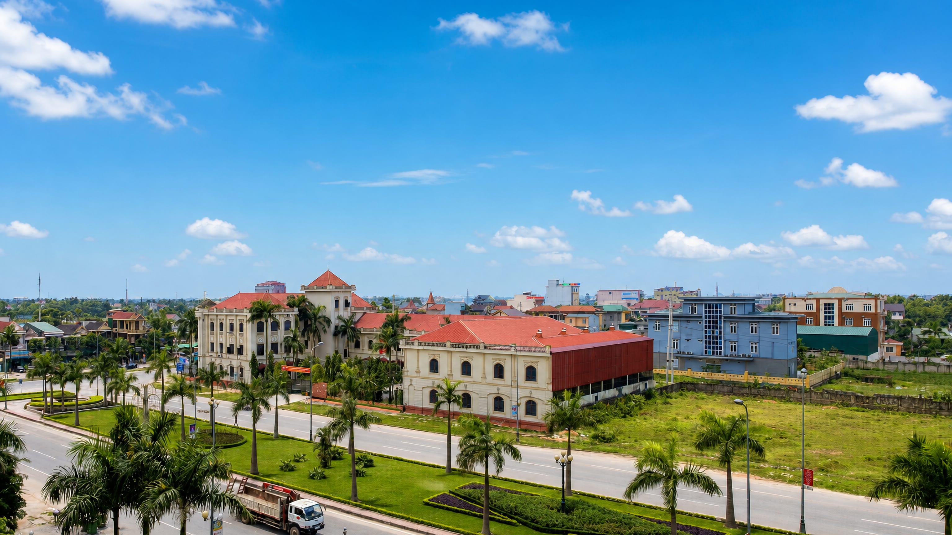 Palm-lined boulevard past colonial-style yellow buildings with red roofs in Hà Tĩnh, Vietnam.