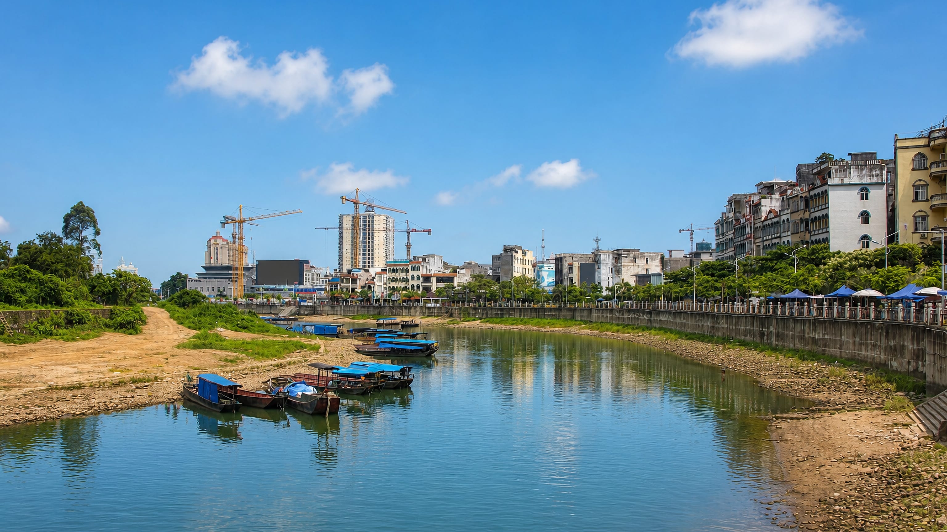 Small boats on the Ka Long River below Mong Cai's riverfront buildings and construction cranes