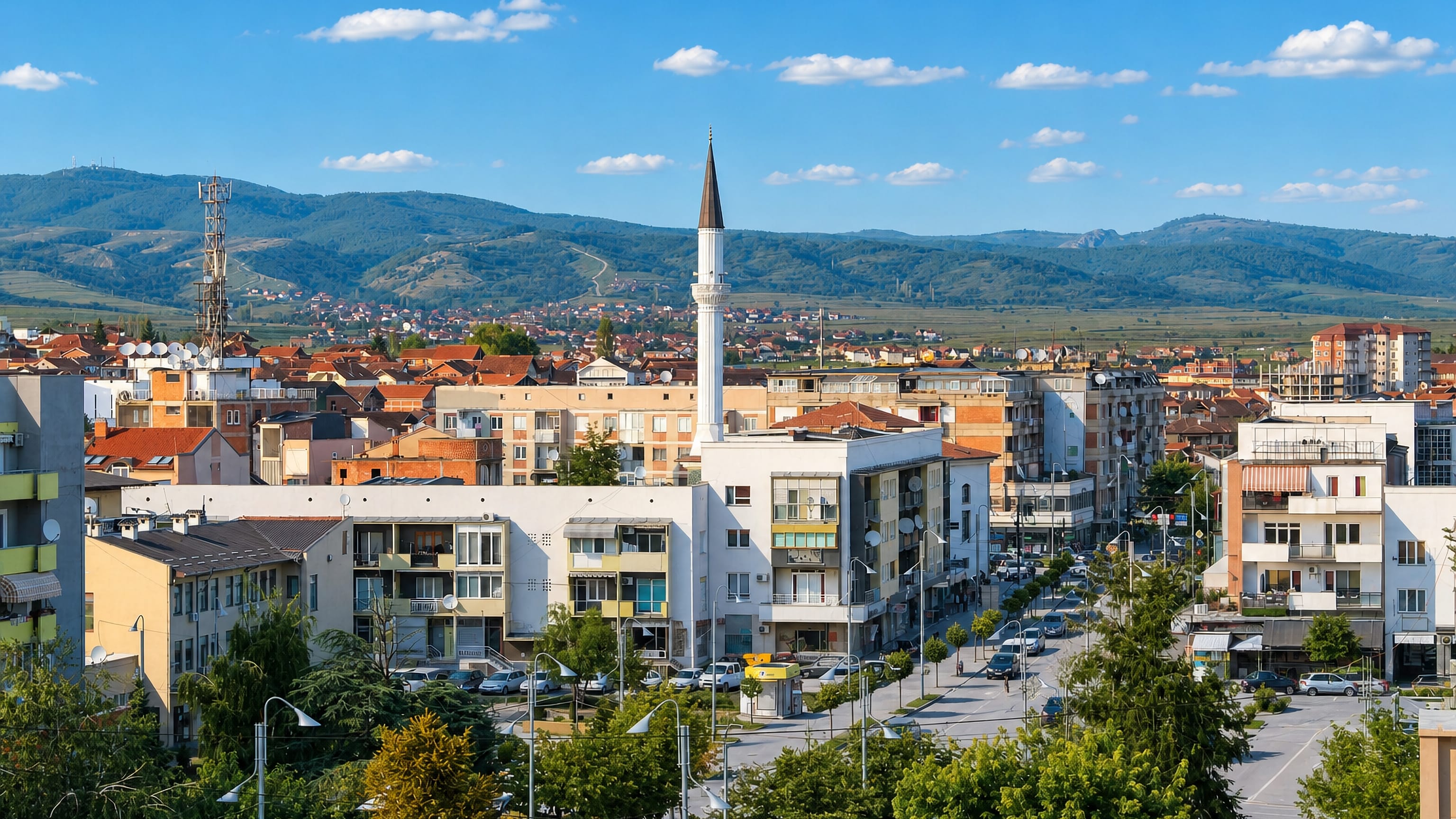 Gjilan's low-rise townscape with a slender mosque minaret and the wooded hills of eastern Kosovo.