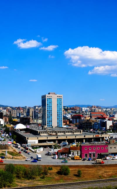 Pristina skyline with the Palace of Youth and Sports and central high-rises under a blue sky.
