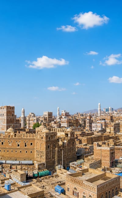 Sanaa's Old City with a tall minaret rising over decorated earthen tower-houses and distant mountains