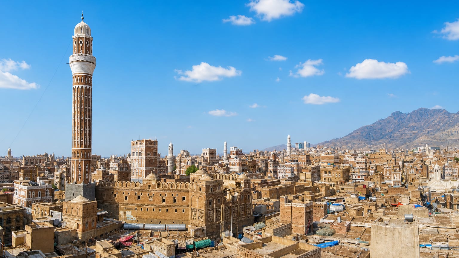 Sanaa's Old City with a tall minaret rising over decorated earthen tower-houses and distant mountains