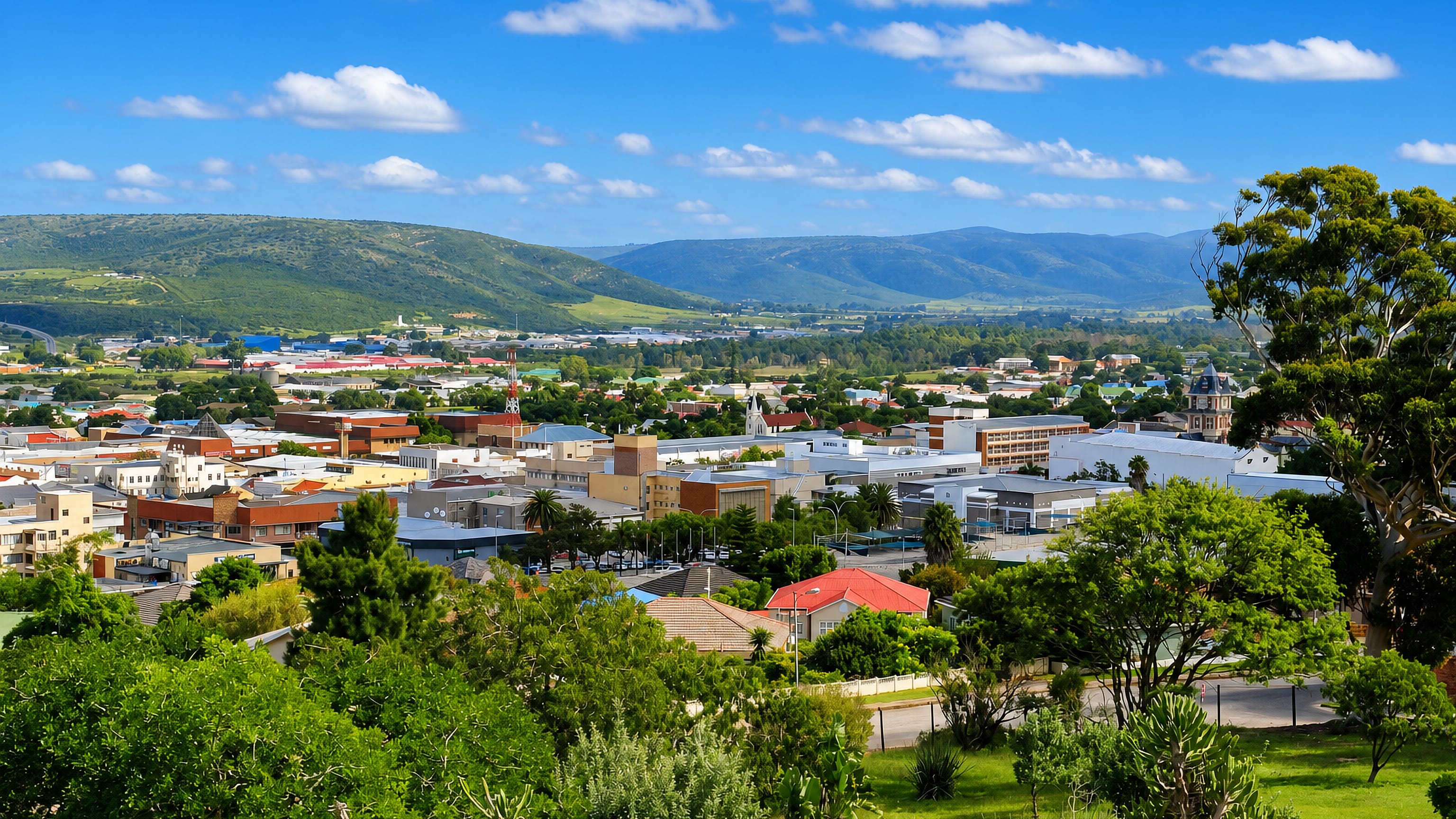 Elevated view over Kariega, South Africa, its low rooftops and church spires backed by green hills.
