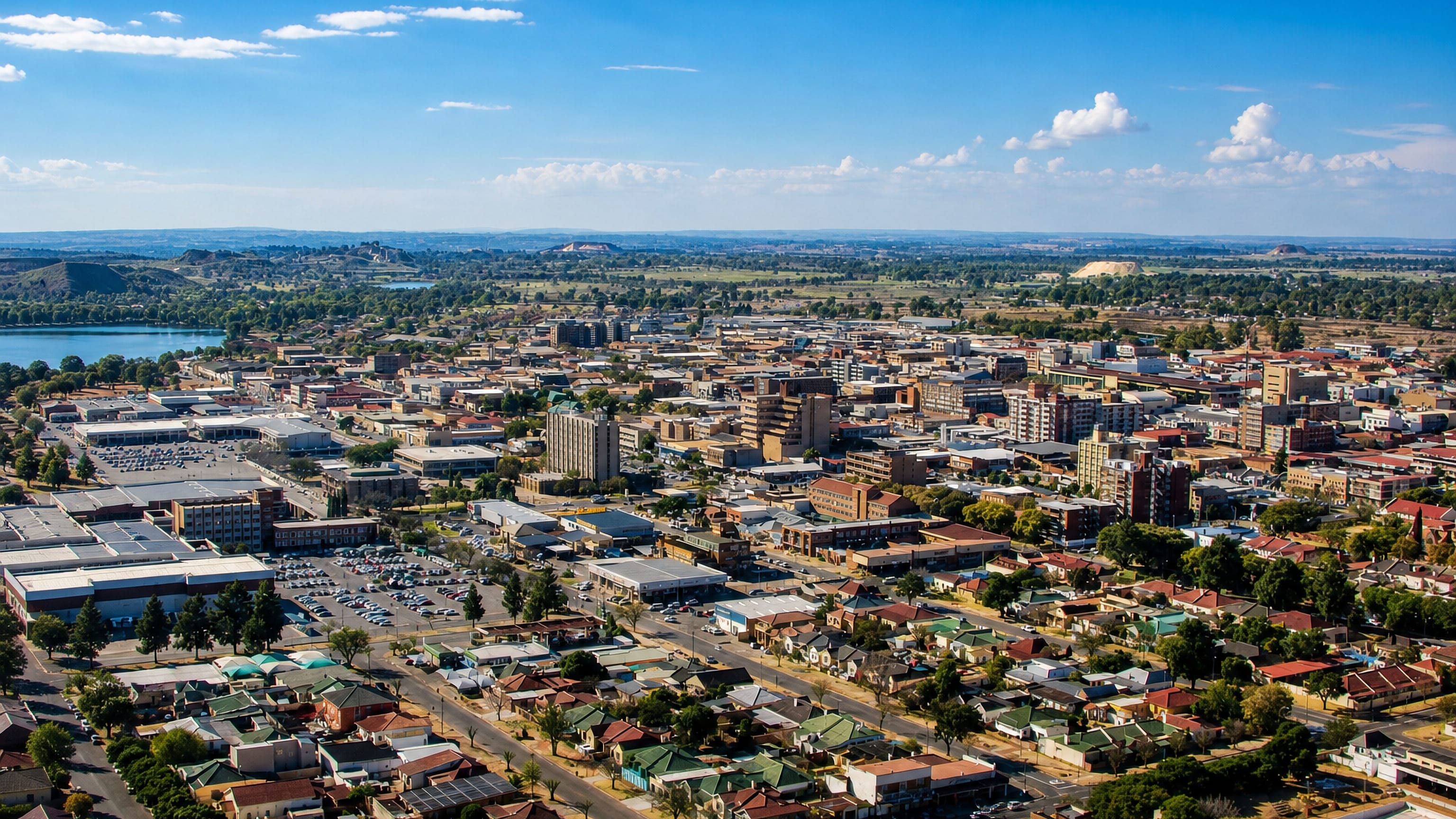 Aerial view of Benoni, South Africa, its low-rise centre beside a lake with mine dumps on the horizon.