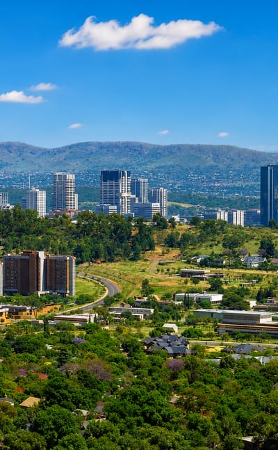 Skyline of Pretoria with its cylindrical tower, CBD high-rises, and purple jacaranda trees in the foreground
