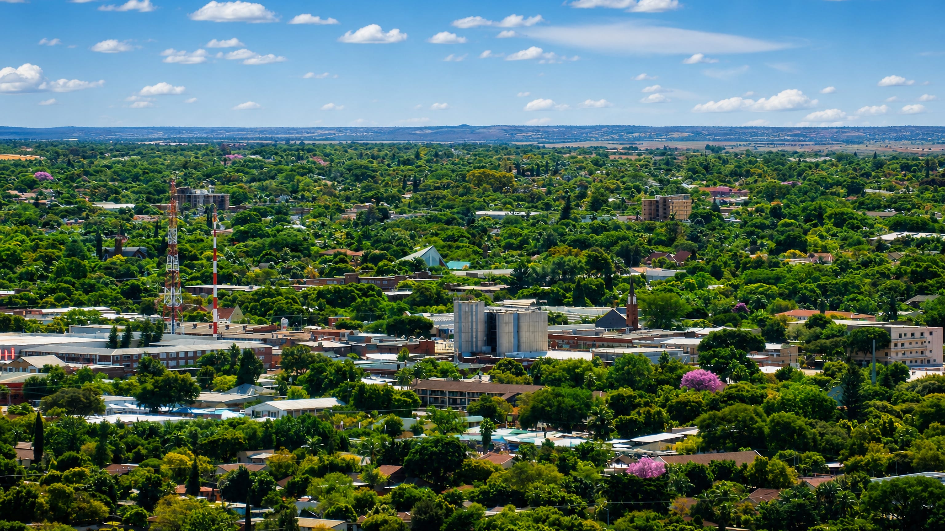 Leafy suburban sprawl of Pretoria North under jacarandas, with a church spire, silos and radio masts.