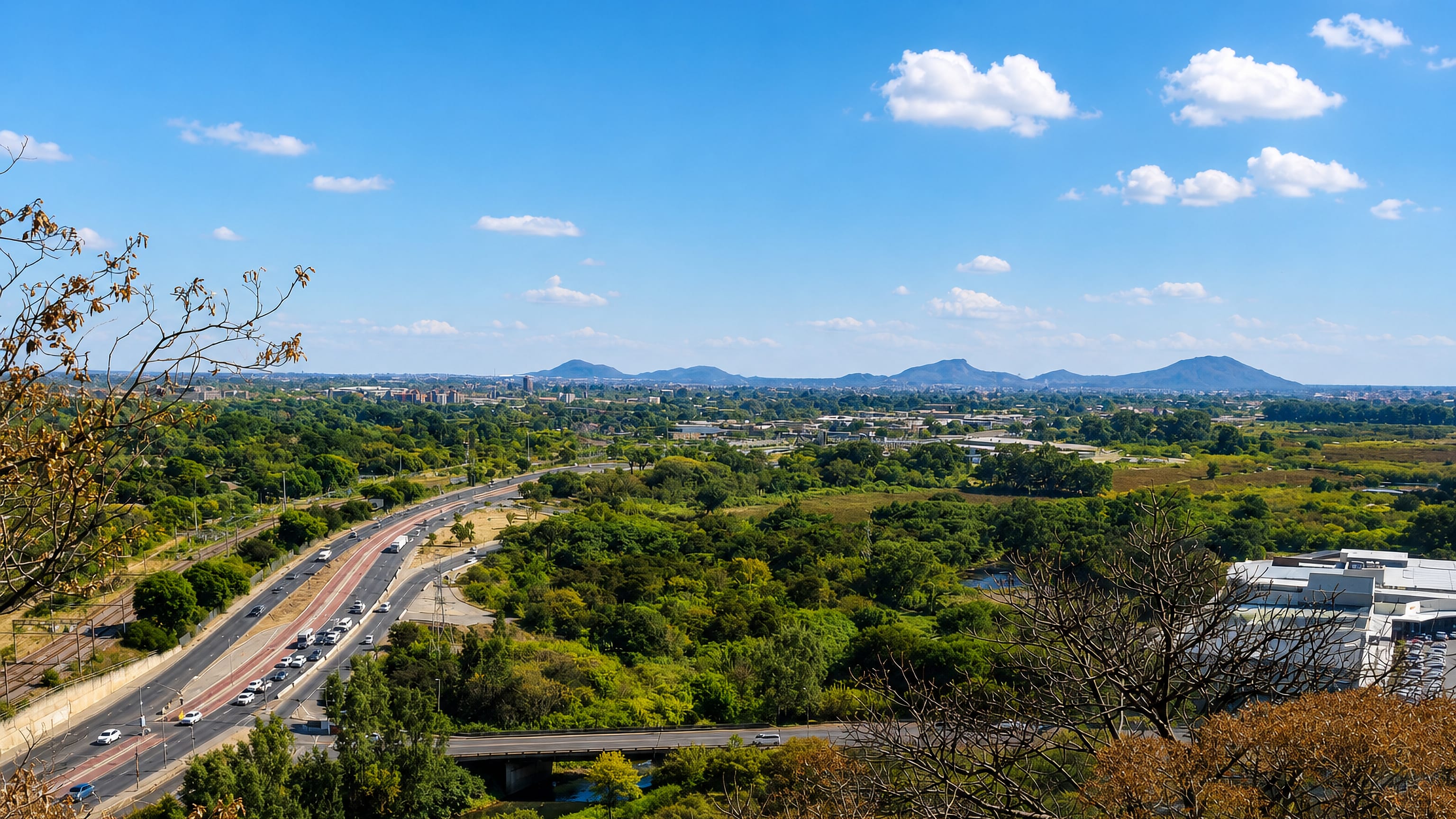 Wonderboom in northern Pretoria, with a highway curving past bushveld toward distant koppies and city buildings.