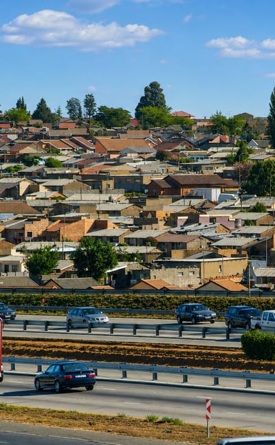Soweto township's dense rooftops rising above a busy multi-lane motorway under a bright sky